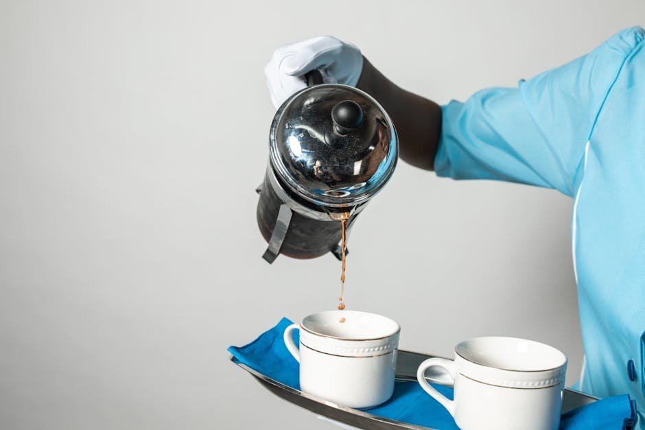 Hand pouring decaf coffee from a French press into a ceramic mug at a kitchen counter