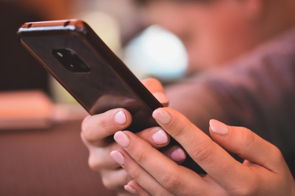Hands holding a basic flip phone with a blurred smartphone and apps in the background