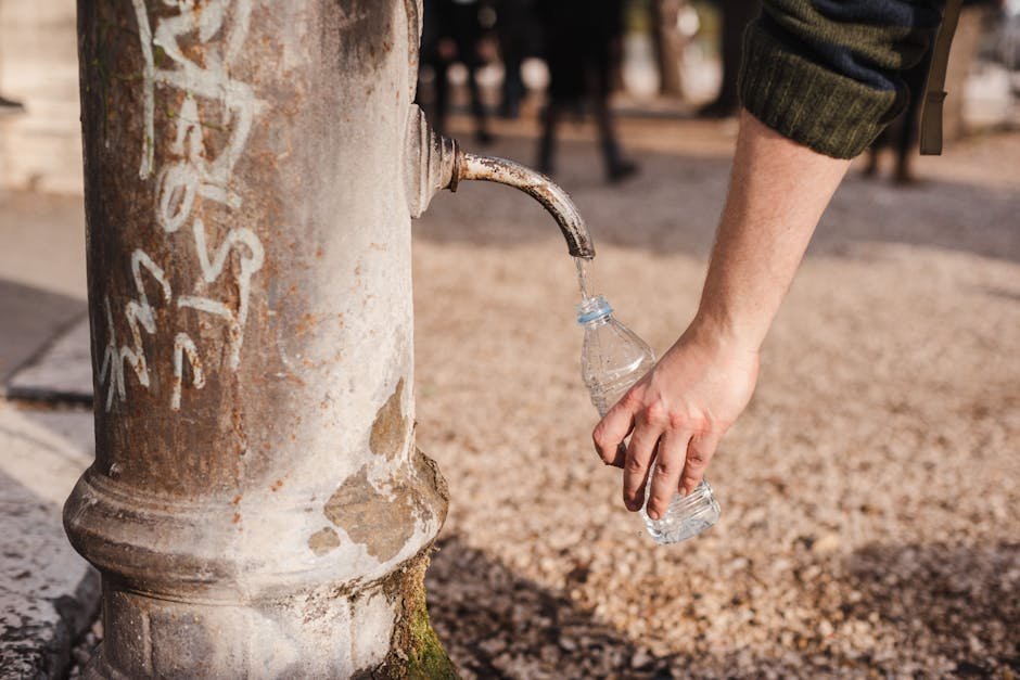 Person filling a reusable water bottle from a kitchen tap during a sunny morning routine
