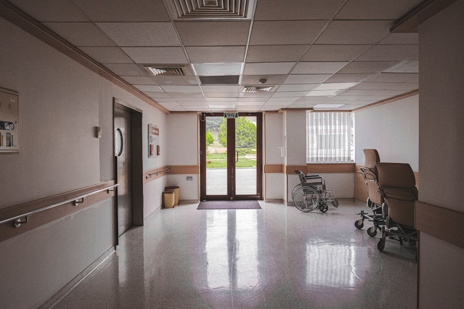 Empty barracks-style hospital corridor with a sunlit window at the end